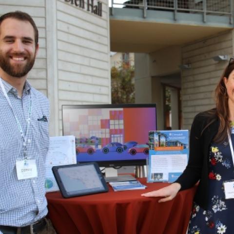 Two people stand by their media display at a tabling event
